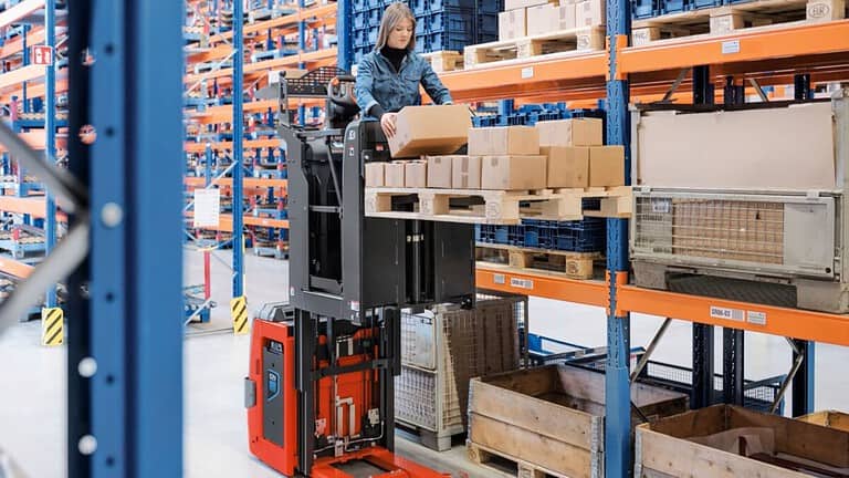 A fe,male worker is running a Linde Order Picker picking up Goods from a high rack.